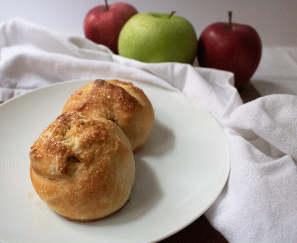apple knishes with coarse sugar on white plate with apples in background